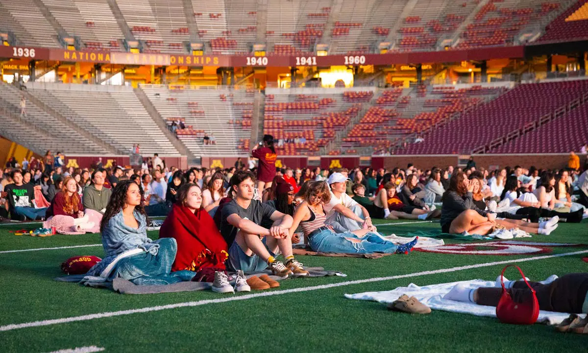 Students sitting on field watching a movie on the jumbotron